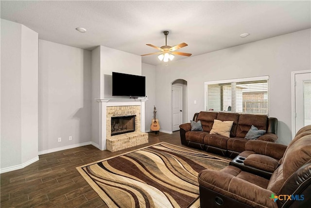 living room with arched walkways, dark wood-style flooring, a fireplace, a ceiling fan, and baseboards