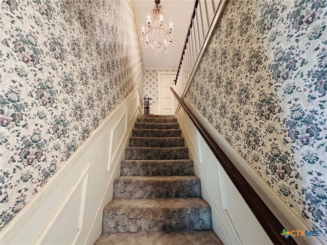 stairs featuring a decorative wall, wallpapered walls, and a chandelier