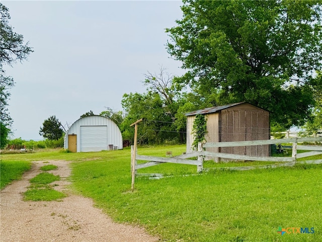 view of yard with a detached garage, fence, an outdoor structure, and driveway