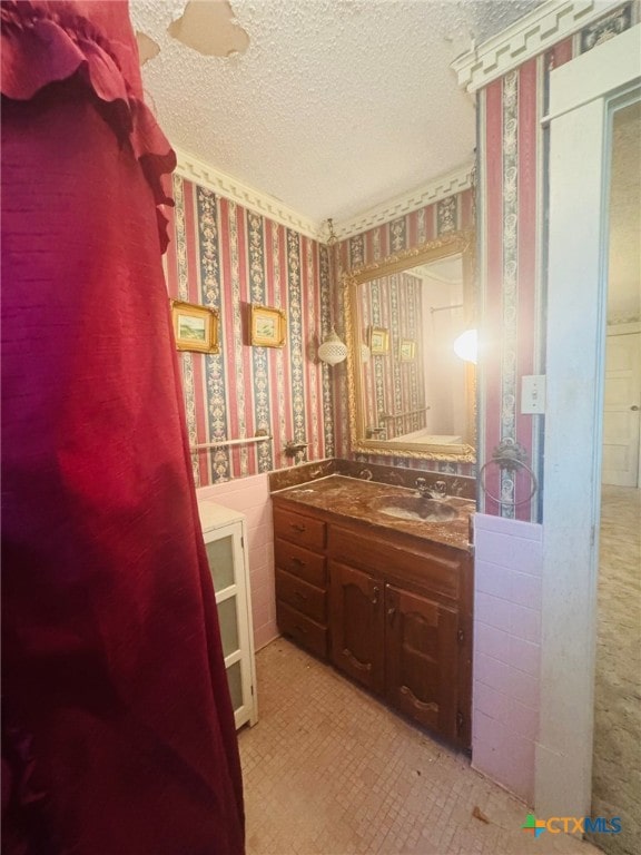 bathroom featuring vanity, wallpapered walls, and a textured ceiling