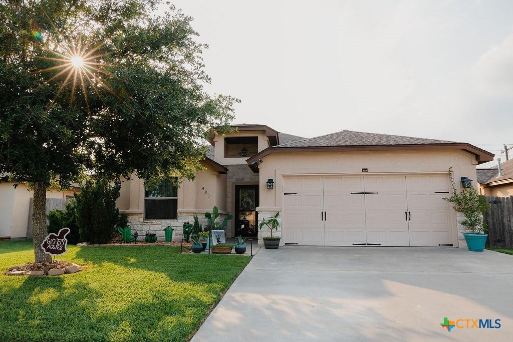 407 Tuscany Dr, Victoria, TX 77904 - view of front facade with an attached garage, driveway, stucco siding, a front yard, and stone siding