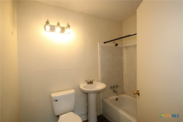 full bathroom with a textured ceiling, toilet, sink, and tiled shower / bath combo