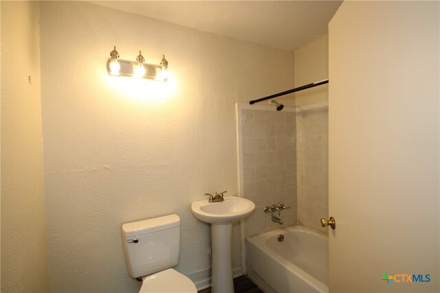 full bathroom with a textured ceiling, toilet, sink, and tiled shower / bath combo