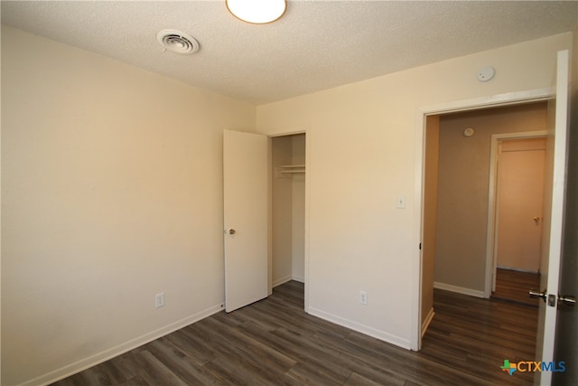 unfurnished bedroom with a closet, a textured ceiling, and dark hardwood / wood-style floors