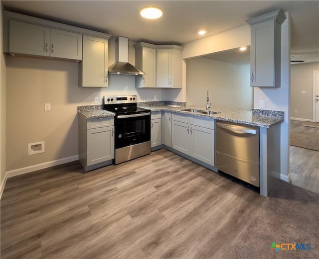 kitchen with wall chimney exhaust hood, gray cabinets, appliances with stainless steel finishes, and a sink