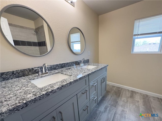 full bath with double vanity, baseboards, wood finish floors, and a sink