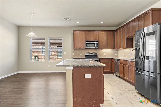 kitchen featuring sink, appliances with stainless steel finishes, light hardwood / wood-style flooring, a kitchen island, and pendant lighting