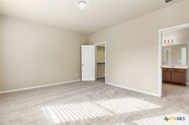 unfurnished bedroom with sink, light carpet, ensuite bathroom, a spacious closet, and a closet