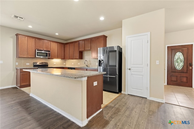 kitchen with stainless steel appliances, light hardwood / wood-style floors, sink, tasteful backsplash, and a kitchen island