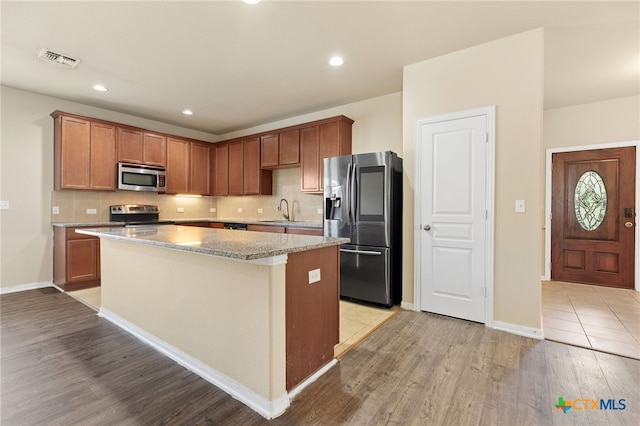13512 Kearns Dr, Pflugerville, TX 78660 - kitchen with stainless steel appliances, a sink, a kitchen island, light wood-type flooring, and decorative backsplash