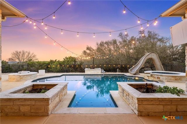 pool at dusk with an in ground hot tub, a fire pit, and a water slide