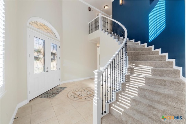 foyer entrance featuring stairway, a high ceiling, baseboards, and light tile patterned flooring