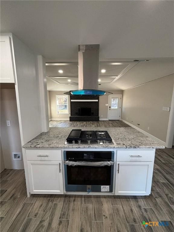 kitchen featuring white cabinetry, island range hood, stainless steel gas cooktop, oven, and light stone counters