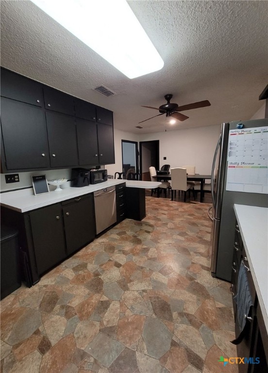kitchen featuring visible vents, a textured ceiling, dark cabinets, stone finish flooring, and appliances with stainless steel finishes