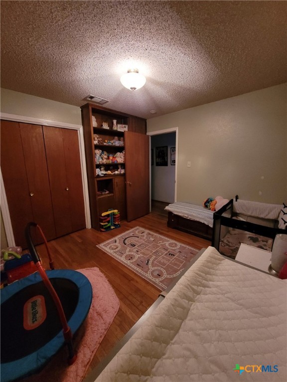 bedroom with visible vents, a textured ceiling, and wood finished floors