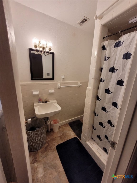 full bath featuring a sink, a chandelier, tile walls, a shower stall, and visible vents