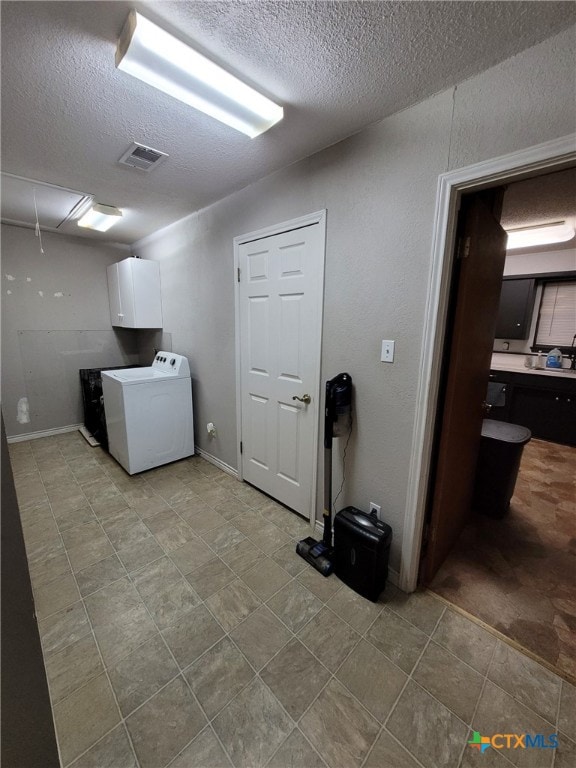 clothes washing area with cabinet space, a sink, a textured ceiling, attic access, and visible vents