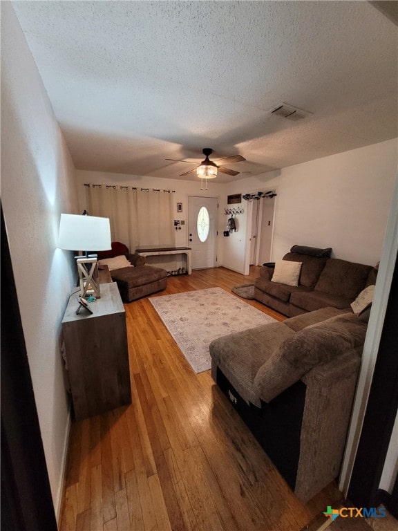 living room featuring visible vents, a textured ceiling, ceiling fan, and light wood finished floors