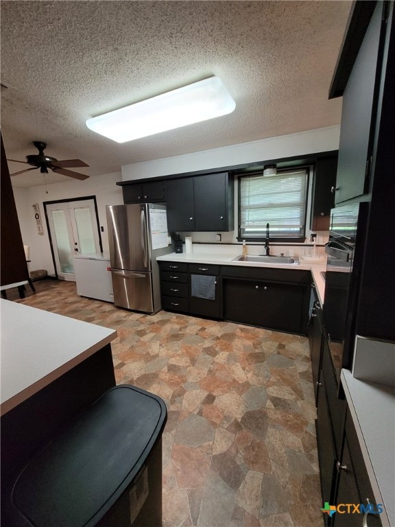 kitchen featuring freestanding refrigerator, black oven, a textured ceiling, dark cabinets, and a sink