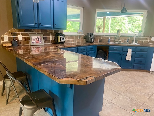 kitchen with blue cabinets, a kitchen breakfast bar, backsplash, and decorative light fixtures