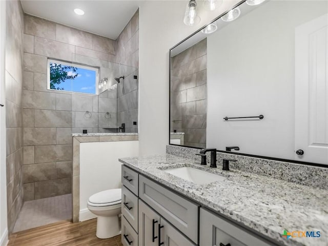 bathroom featuring toilet, vanity, tiled shower, and hardwood / wood-style flooring