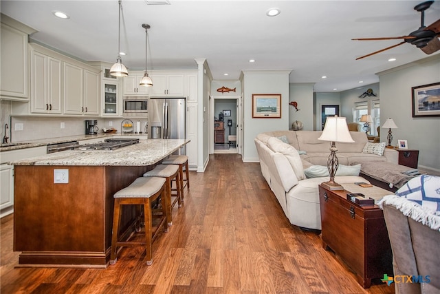 kitchen featuring appliances with stainless steel finishes, light stone countertops, hanging light fixtures, a center island, and dark wood-type flooring