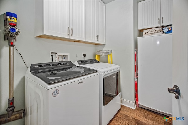 clothes washing area with cabinets, hardwood / wood-style flooring, and washing machine and dryer