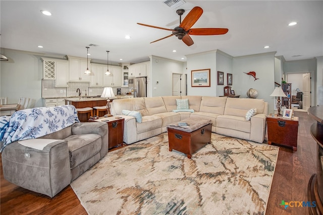 living room with ornamental molding, dark hardwood / wood-style floors, ceiling fan, and sink