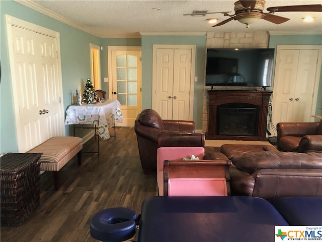 living room with dark wood-type flooring, a textured ceiling, ornamental molding, ceiling fan, and a fireplace