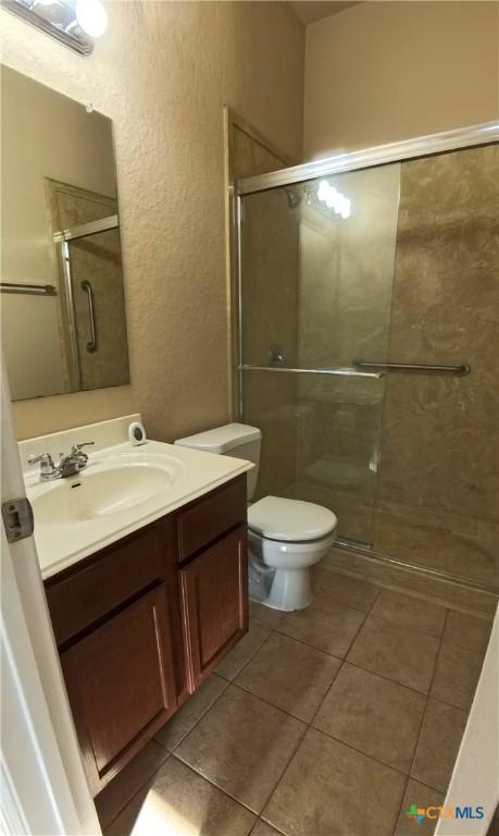 8710 Jogeva Way, San Antonio, TX 78251 - full bathroom featuring a stall shower, tile patterned flooring, a textured wall, toilet, and vanity