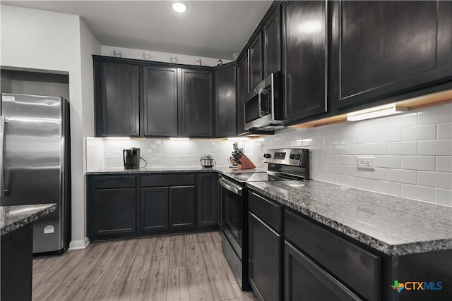 7005 Mcgregor Loop, Killeen, TX 76549 - kitchen with appliances with stainless steel finishes, dark stone counters, light wood-style flooring, dark cabinetry, and decorative backsplash