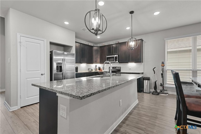 7005 Mcgregor Loop, Killeen, TX 76549 - kitchen featuring stainless steel appliances, light wood-style floors, light stone counters, dark brown cabinetry, and an island with sink
