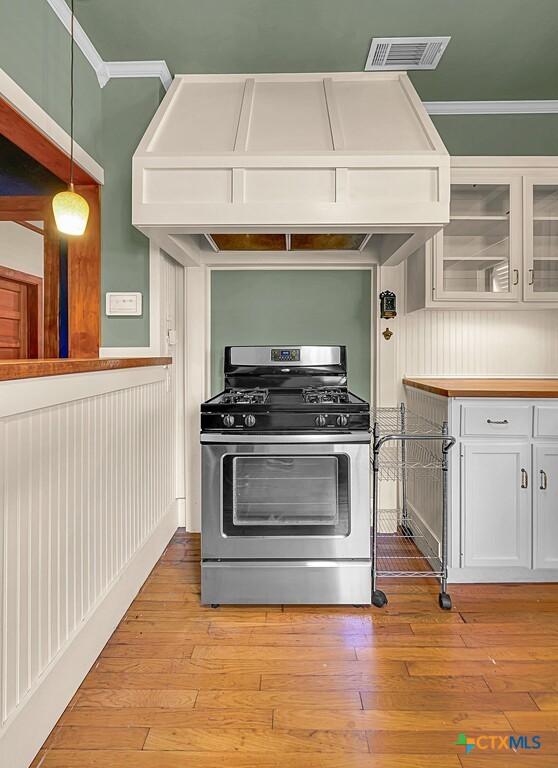 905 N 33rd St, Waco, TX 76707 - kitchen with stainless steel gas range oven, white cabinetry, premium range hood, glass insert cabinets, and hanging light fixtures