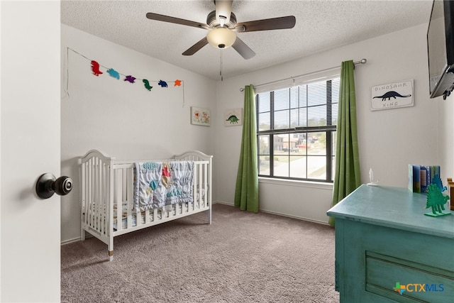 carpeted bedroom with ceiling fan, a textured ceiling, and a nursery area