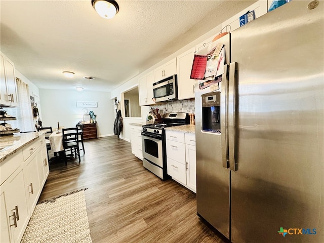 kitchen featuring light stone countertops, stainless steel appliances, tasteful backsplash, white cabinets, and hardwood / wood-style flooring