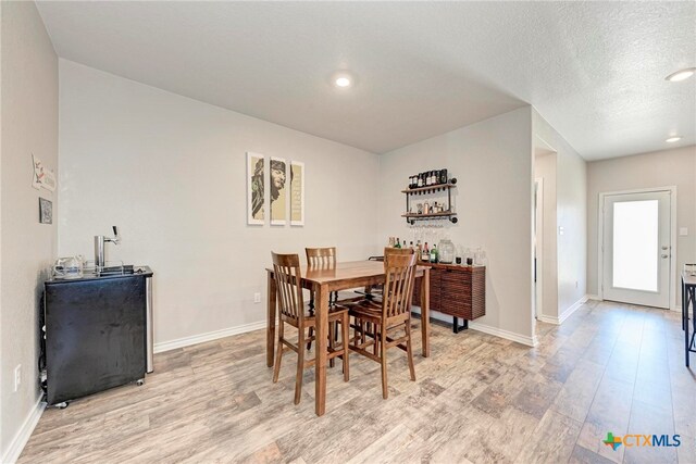 dining space featuring a textured ceiling, indoor bar, and light hardwood / wood-style flooring