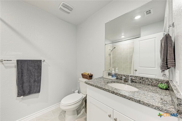 bathroom featuring toilet, a tile shower, vanity, and tile patterned floors