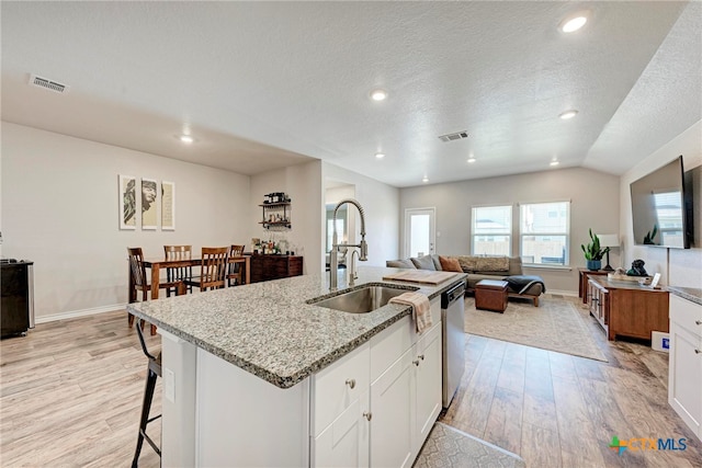 kitchen with sink, an island with sink, light hardwood / wood-style flooring, white cabinets, and vaulted ceiling