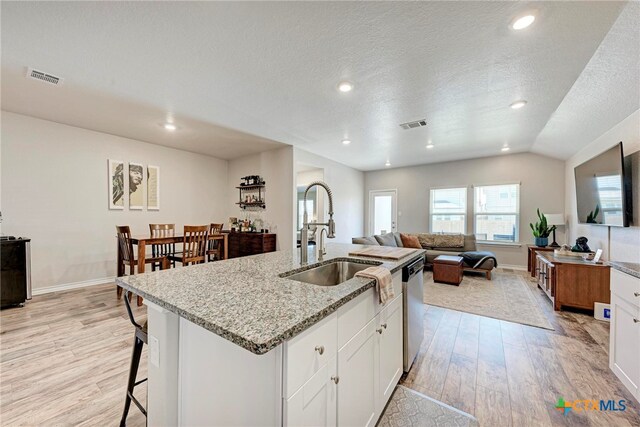 kitchen with sink, an island with sink, light hardwood / wood-style flooring, white cabinets, and vaulted ceiling