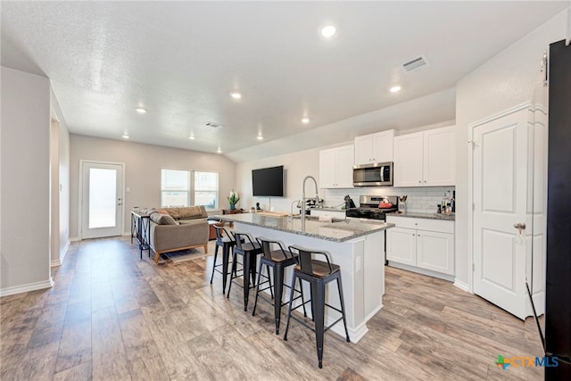 kitchen featuring stainless steel appliances, light hardwood / wood-style floors, a kitchen island with sink, light stone countertops, and white cabinetry