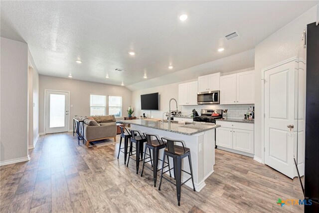 kitchen featuring stainless steel appliances, light hardwood / wood-style floors, a kitchen island with sink, light stone countertops, and white cabinetry