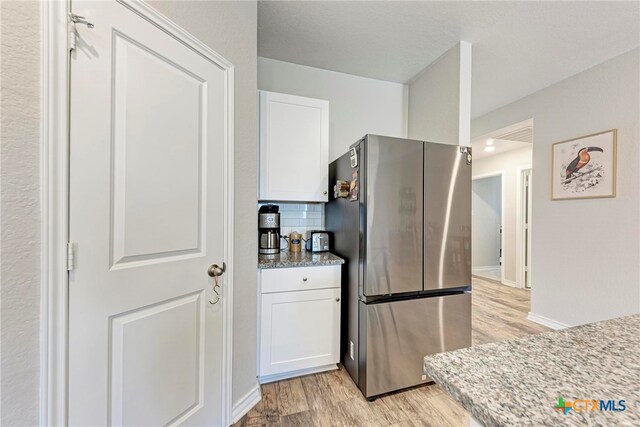 kitchen featuring white cabinets, decorative backsplash, light hardwood / wood-style flooring, and stainless steel fridge