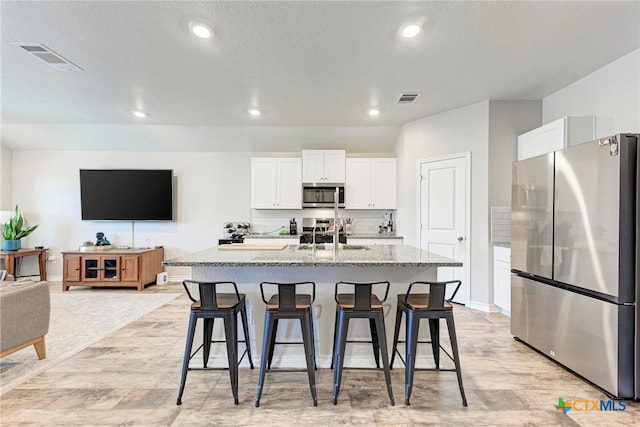 kitchen with a center island with sink, a breakfast bar, appliances with stainless steel finishes, backsplash, and white cabinets