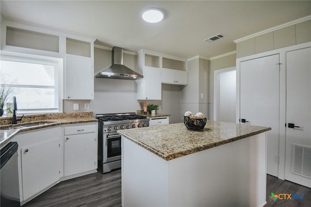 kitchen with appliances with stainless steel finishes, white cabinets, a sink, wall chimney range hood, and a kitchen island