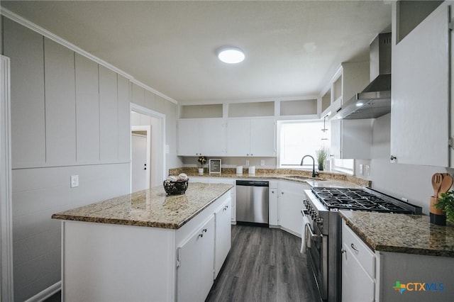 kitchen with a center island, appliances with stainless steel finishes, white cabinets, a sink, and wall chimney range hood