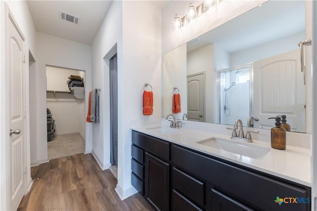 full bathroom featuring wood finished floors, a shower stall, a spacious closet, double vanity, and baseboards
