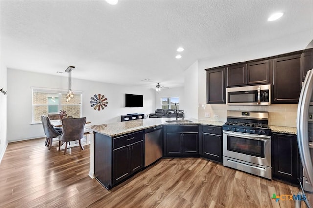 kitchen featuring stainless steel appliances, a peninsula, light wood-type flooring, light stone countertops, and open floor plan