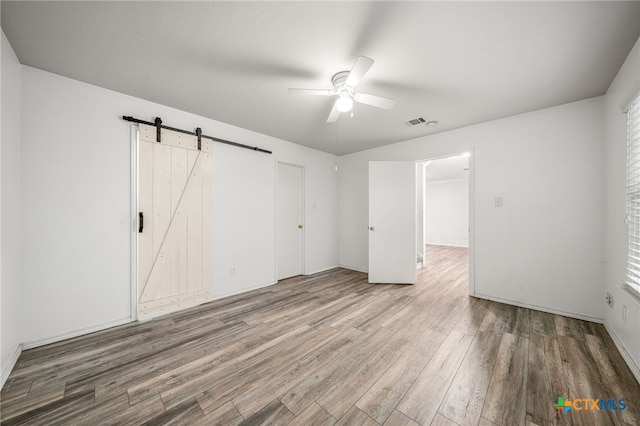 unfurnished bedroom with a barn door, hardwood / wood-style floors, and ceiling fan