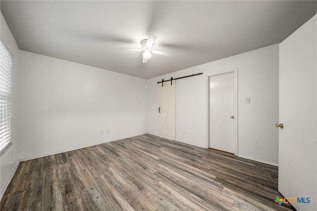 unfurnished bedroom featuring wood-type flooring, a barn door, and ceiling fan