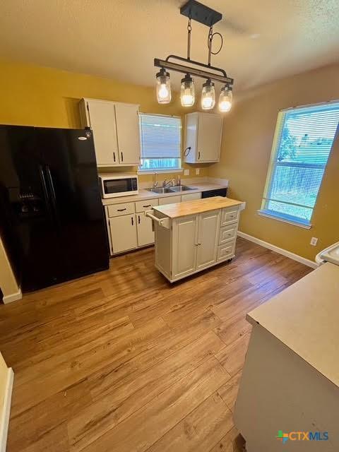 4306 Menard Dr, Killeen, TX 76549 - kitchen with black refrigerator with ice dispenser, white microwave, a sink, light countertops, and white cabinetry